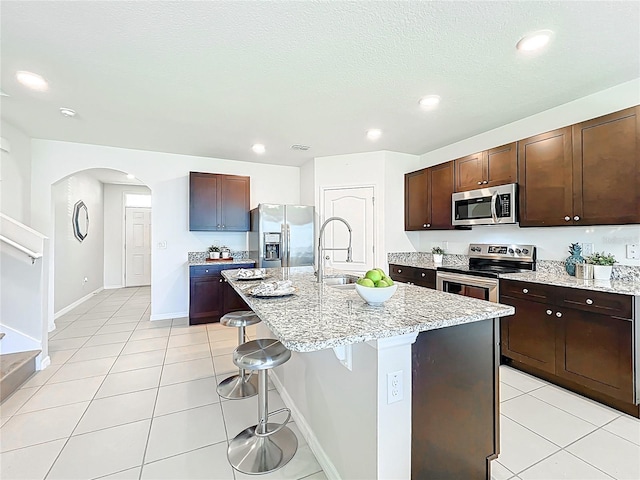 3279 Landing Vw, Tavares, FL 32778 - kitchen with arched walkways, a kitchen bar, light stone countertops, light tile patterned flooring, and stainless steel appliances