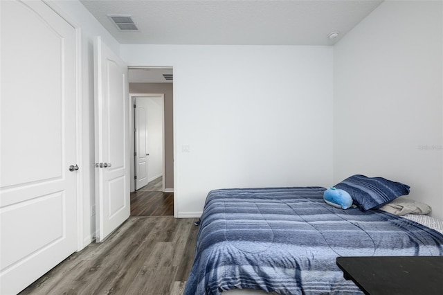 bedroom featuring a textured ceiling, wood finished floors, visible vents, and baseboards