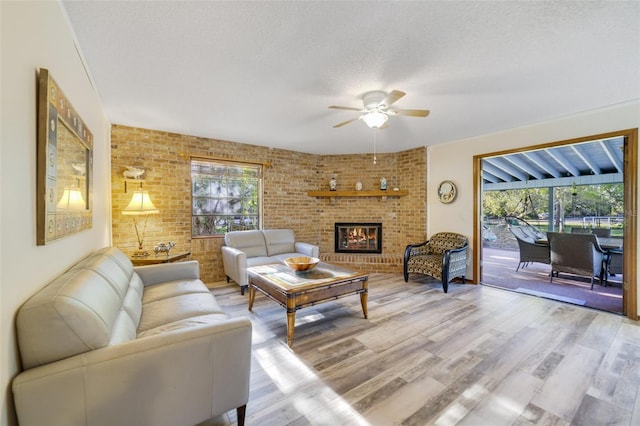 living area with light wood finished floors, brick wall, a brick fireplace, ceiling fan, and a textured ceiling