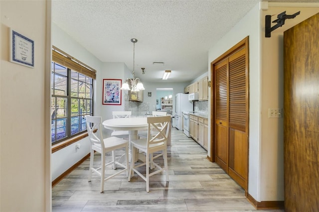 dining area with a notable chandelier, light wood-style flooring, a textured ceiling, and baseboards