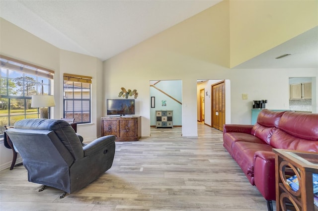 living area with visible vents, baseboards, high vaulted ceiling, and light wood finished floors