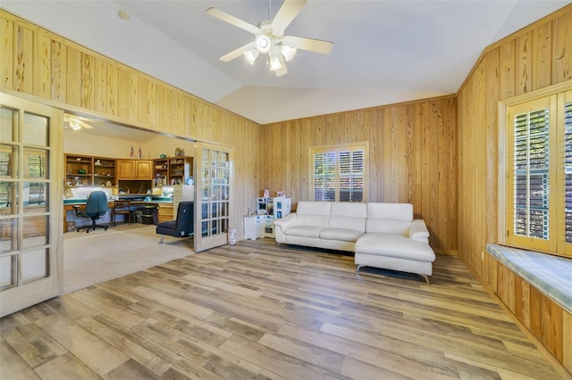 living room with ceiling fan, wood walls, and vaulted ceiling