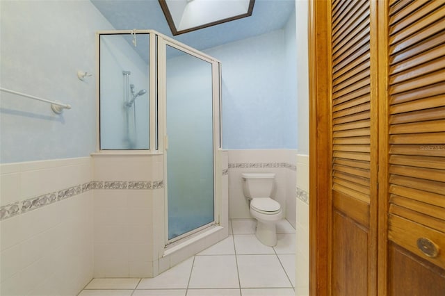 full bathroom featuring tile patterned flooring, a wainscoted wall, a shower stall, and a closet