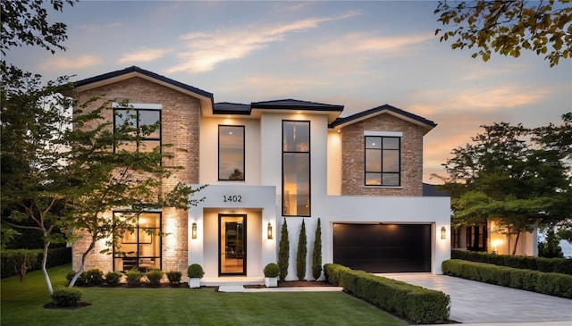 view of front of house with stucco siding, concrete driveway, a front yard, an attached garage, and brick siding