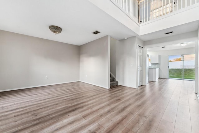 empty room featuring stairway, wood finished floors, visible vents, and baseboards