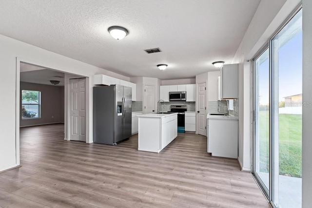 kitchen featuring visible vents, an island with sink, a sink, stainless steel appliances, and light wood-style floors