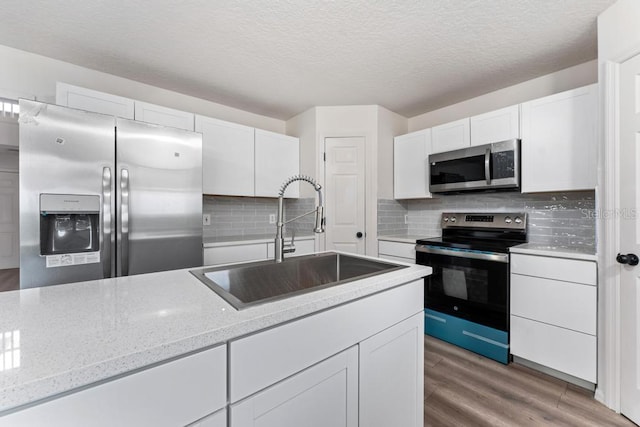 kitchen featuring tasteful backsplash, stainless steel appliances, light wood-style floors, white cabinetry, and a sink