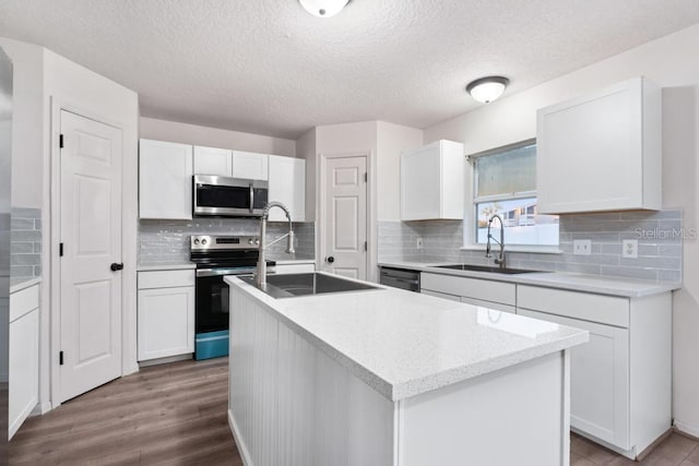 kitchen with a center island with sink, a sink, wood finished floors, appliances with stainless steel finishes, and white cabinets