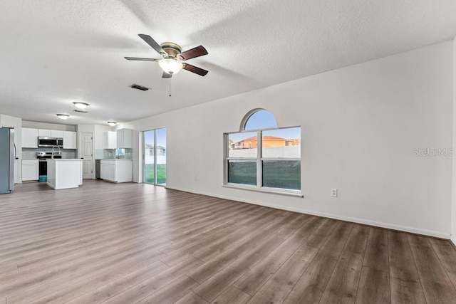 unfurnished living room featuring a textured ceiling, wood finished floors, visible vents, and ceiling fan