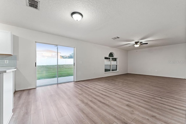 unfurnished living room featuring visible vents, light wood-style floors, a ceiling fan, and a textured ceiling