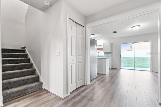 staircase featuring visible vents, a textured ceiling, baseboards, and wood finished floors