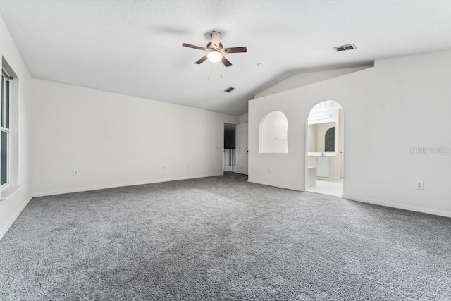 carpeted empty room with baseboards, visible vents, arched walkways, ceiling fan, and vaulted ceiling