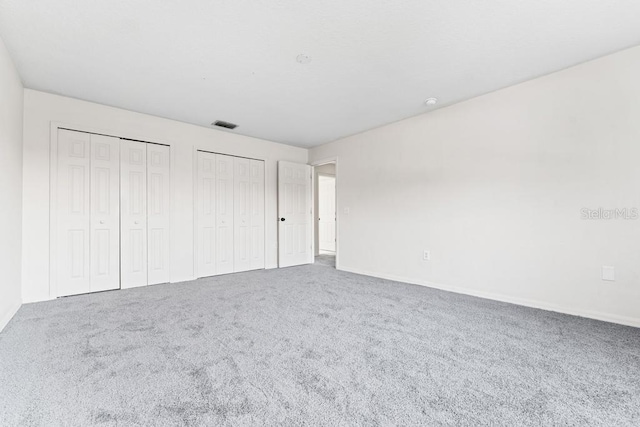 unfurnished bedroom with visible vents, two closets, and carpet floors