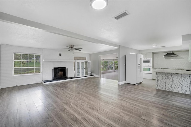 unfurnished living room with visible vents, wood finished floors, brick wall, a brick fireplace, and ceiling fan