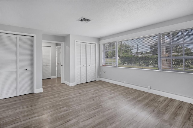 unfurnished bedroom with wood finished floors, baseboards, visible vents, multiple closets, and a textured ceiling