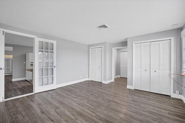 unfurnished bedroom with visible vents, baseboards, multiple closets, and wood finished floors