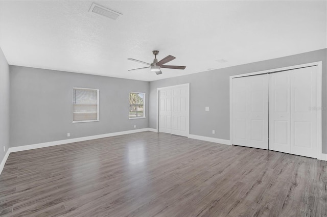 unfurnished bedroom with wood finished floors, visible vents, baseboards, multiple closets, and a textured ceiling