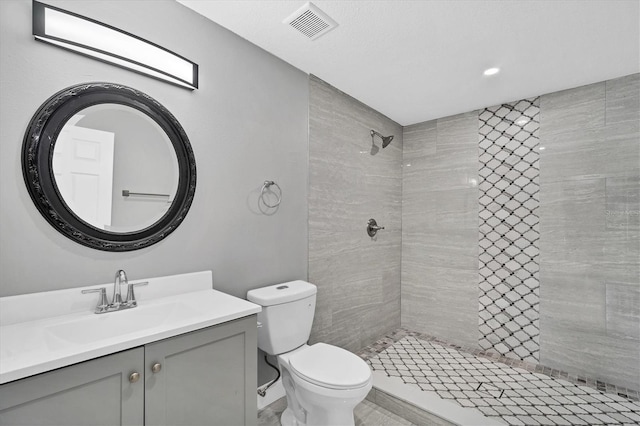 bathroom featuring a tile shower, visible vents, toilet, and vanity