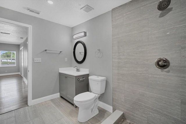 bathroom with visible vents, toilet, baseboards, tiled shower, and vanity