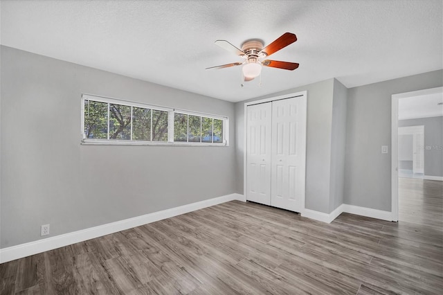 unfurnished bedroom featuring a closet, baseboards, a textured ceiling, and wood finished floors