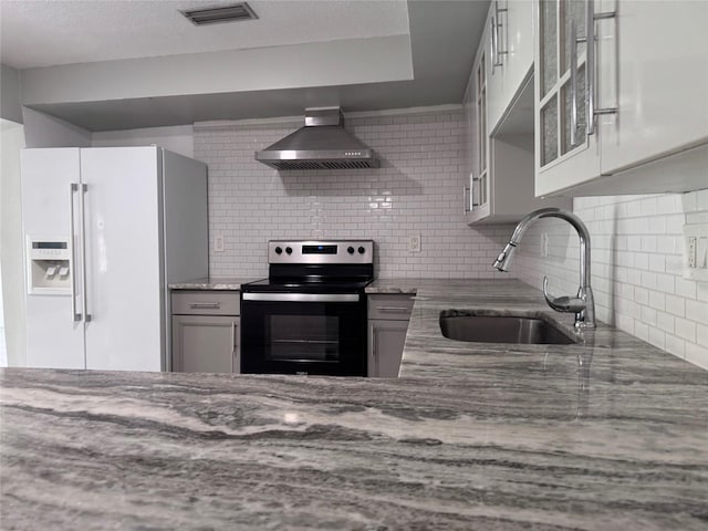 kitchen with visible vents, electric range, a sink, white fridge with ice dispenser, and wall chimney range hood