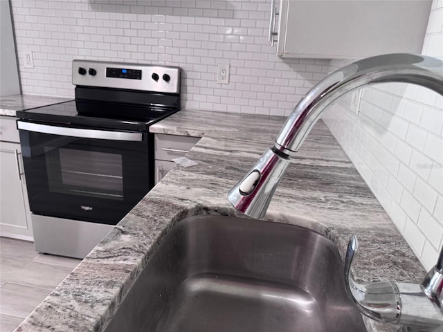 kitchen with decorative backsplash, light stone countertops, stainless steel electric range oven, and a sink