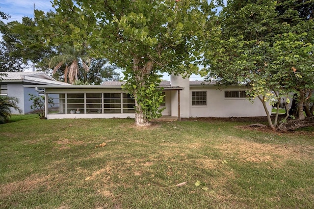 rear view of property with stucco siding, a yard, and a sunroom