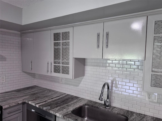 kitchen with a sink, glass insert cabinets, backsplash, and dark stone countertops