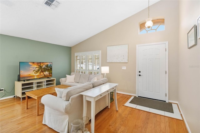 living area with visible vents, lofted ceiling, light wood-style floors, and baseboards