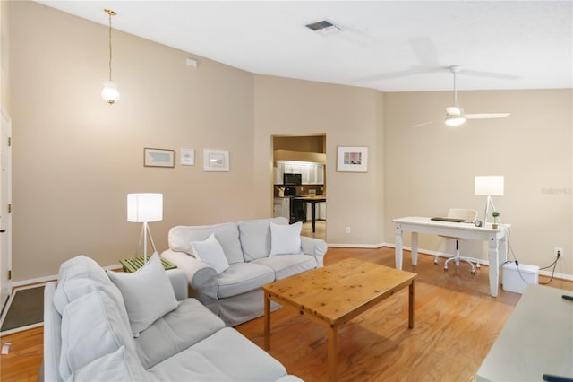 living area featuring visible vents, baseboards, vaulted ceiling, light wood-style flooring, and a ceiling fan