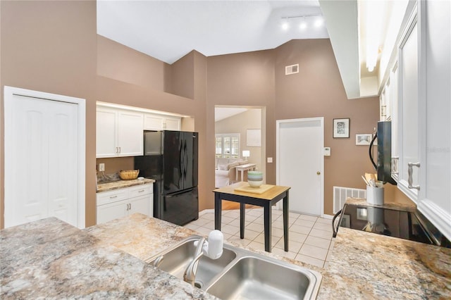 kitchen featuring visible vents, lofted ceiling, freestanding refrigerator, white cabinetry, and a sink