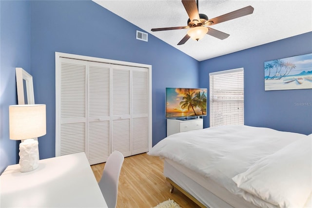 bedroom featuring visible vents, lofted ceiling, a closet, a textured ceiling, and light wood-type flooring