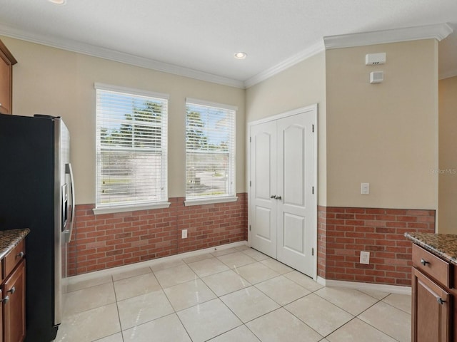 kitchen with dark stone countertops, stainless steel fridge, brick wall, and ornamental molding