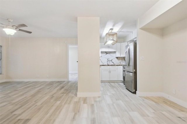 unfurnished living room featuring a sink, baseboards, light wood-style floors, and a ceiling fan