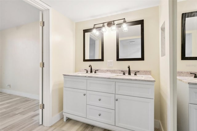 bathroom featuring double vanity, wood finished floors, baseboards, and a sink