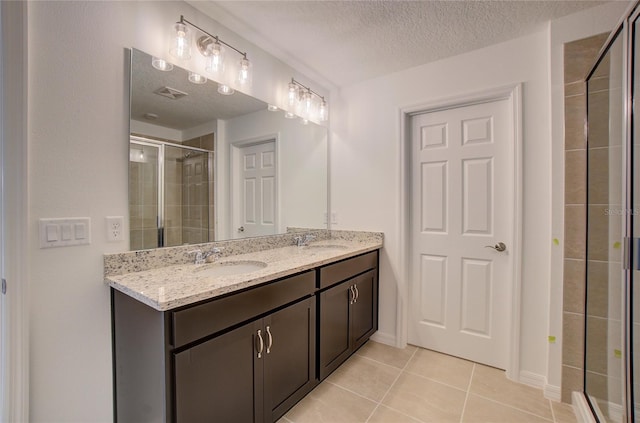 full bath with double vanity, a sink, tile patterned flooring, a shower stall, and a textured ceiling