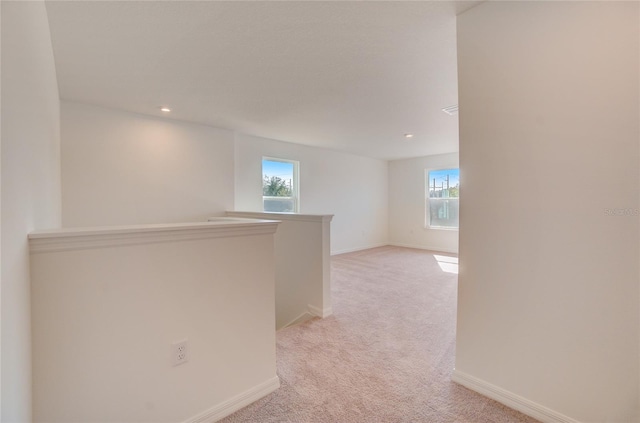 corridor with baseboards, an upstairs landing, light colored carpet, and plenty of natural light