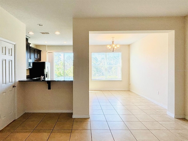 kitchen with a kitchen breakfast bar, dark countertops, fridge, light tile patterned floors, and baseboards