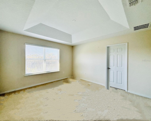 spare room featuring a tray ceiling, visible vents, and baseboards