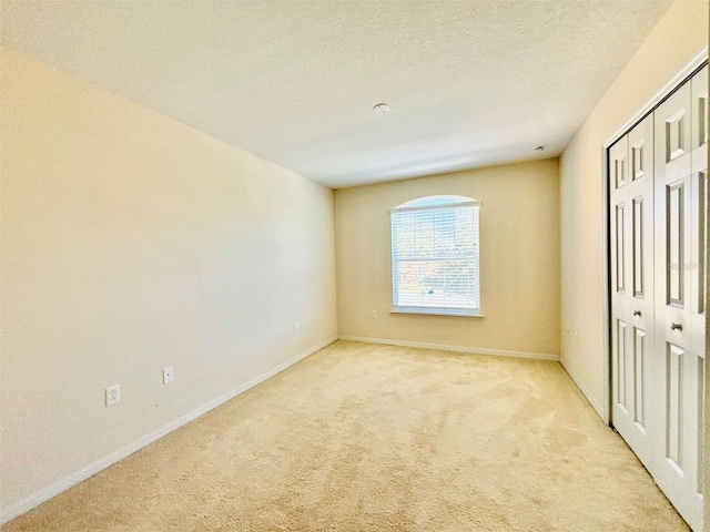 unfurnished bedroom with light carpet, baseboards, a textured ceiling, and a closet