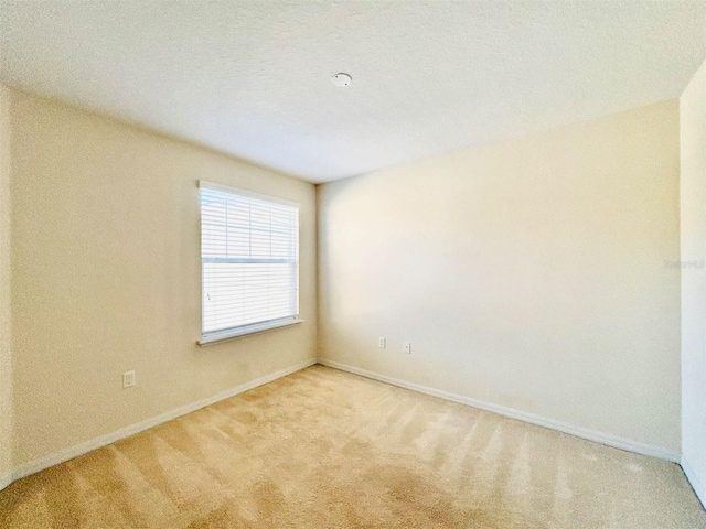 spare room with light carpet, a textured ceiling, and baseboards