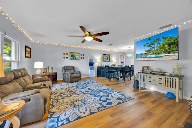 living room featuring visible vents, baseboards, wood finished floors, and a ceiling fan