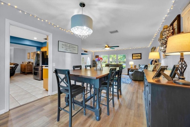 dining space featuring ceiling fan with notable chandelier, light wood-style floors, visible vents, and baseboards