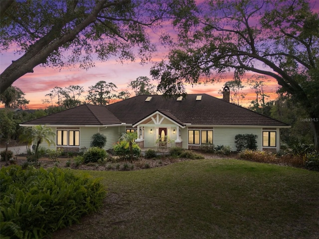 view of front of home featuring a tile roof, a lawn, and a chimney