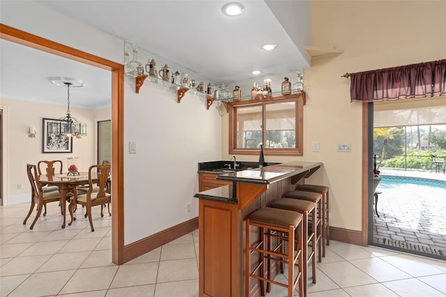 kitchen featuring light tile patterned flooring, brown cabinets, a breakfast bar area, and a sink