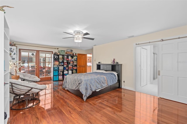 bedroom featuring visible vents, a ceiling fan, wood finished floors, a barn door, and french doors