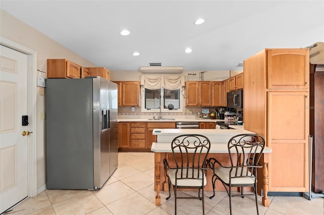 kitchen with light countertops, a peninsula, a kitchen breakfast bar, stainless steel appliances, and a sink