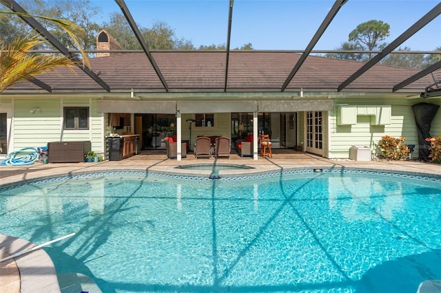 outdoor pool with glass enclosure, an in ground hot tub, and a patio area