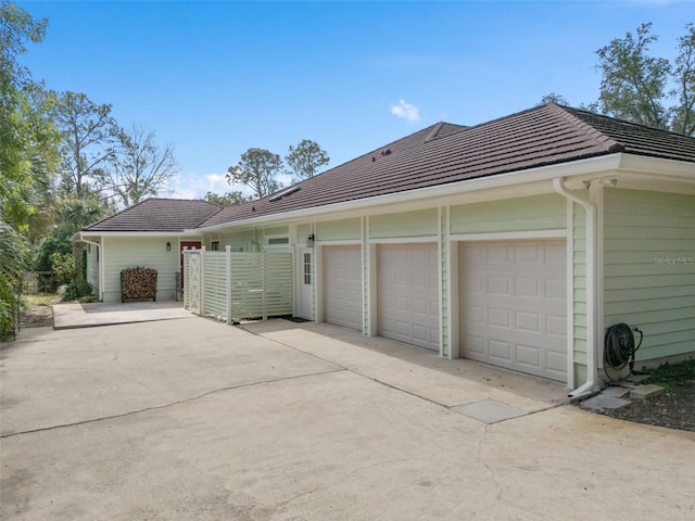 view of property exterior featuring driveway, a tile roof, and an attached garage