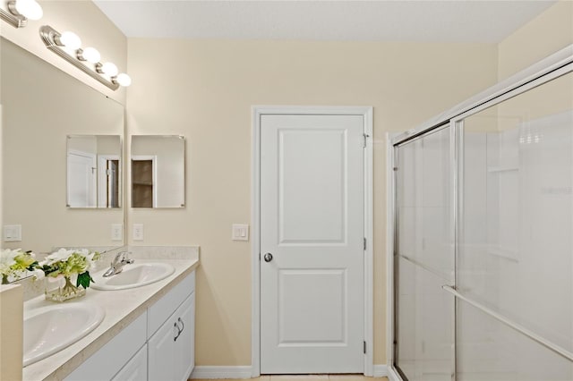 full bathroom with a shower stall, double vanity, baseboards, and a sink